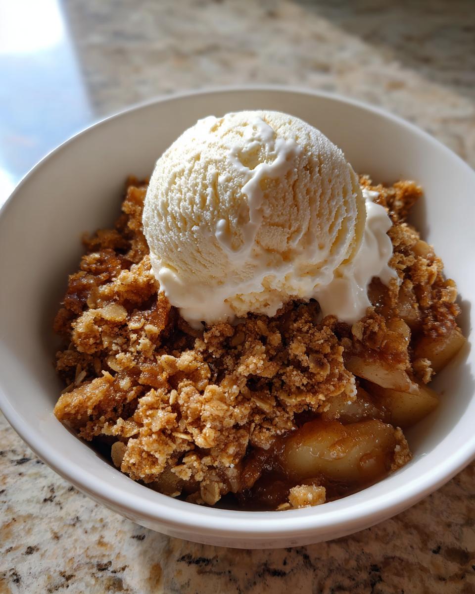 A warm serving of homemade apple crisp topped with a melting scoop of vanilla ice cream in a white bowl.