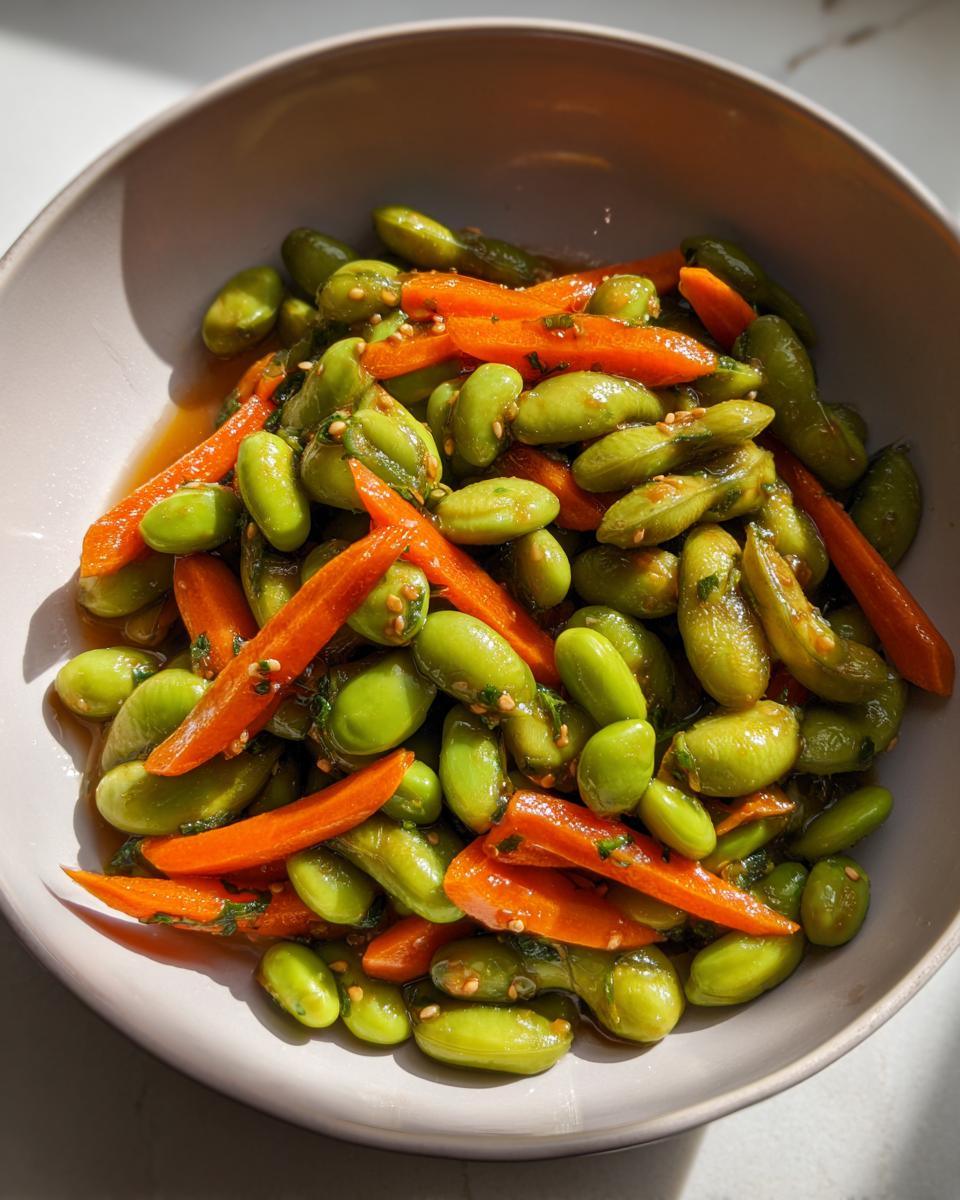 Close-up of a bowl filled with bright green edamame salad mixed with bright orange, thinly sliced carrots and sesame seeds.