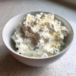 A white bowl filled with chunky, creamy blue cheese dip featuring visible crumbles of blue mold.