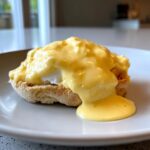 Close-up of Eggs Benedict topped with rich, creamy hollandaise sauce dripping down the side.