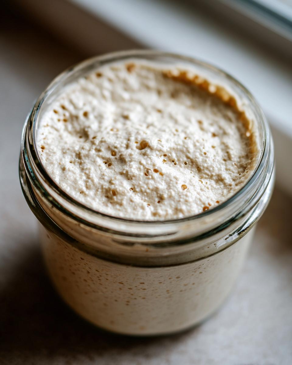 Close-up of an active, bubbly sourdough starter peaking over the rim of a glass jar, showing signs of fermentation.