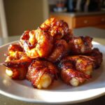 A pile of perfectly cooked, glazed bacon wrapped shrimp served on a white plate, glistening in the sunlight.