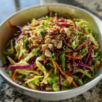 A vibrant bowl of Asian-style cabbage salad topped with peanuts, sesame seeds, and a savory dressing.