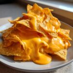 A pile of tortilla chips completely smothered in thick, bright orange nacho cheese sauce.