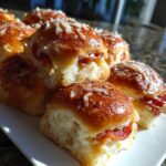 A stack of freshly baked pizza sliders topped with melted cheese and herbs, showing the soft interior.