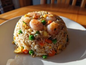 A dome-shaped serving of shrimp fried rice mixed with peas and carrots, topped with succulent cooked shrimp.