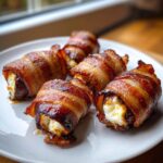 Five crispy, glazed, bacon-wrapped stuffed dates filled with creamy white cheese, served on a white plate.