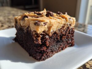 Close-up of a moist, dark chocolate banana bread brownies slice topped with peanut butter frosting and mini chocolate chips.