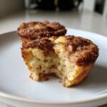 A close-up of a delicious french toast muffin with a bite taken out, showing the soft interior and cinnamon sugar topping.
