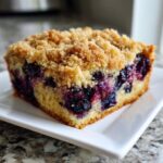A close-up of a moist slice of blueberry breakfast cake topped with a thick, golden streusel crumb topping.
