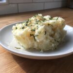 A generous scoop of creamy Boursin mashed potatoes topped with melted butter and fresh chopped parsley.