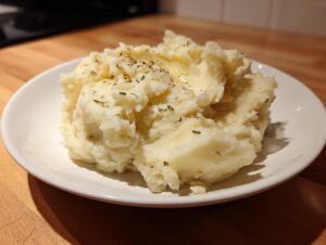 A generous serving of creamy Boursin mashed potatoes topped with melted butter and dried herbs on a white plate.