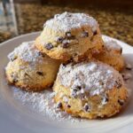 A stack of four freshly baked cannoli cookies loaded with mini chocolate chips and dusted heavily with powdered sugar.