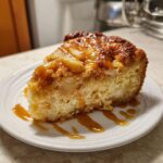 A close-up of a moist slice of caramel apple dump cake drizzled generously with extra caramel sauce.