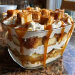 Close-up of a layered caramel apple trifle featuring cake, cream, and caramel sauce dripping down the glass bowl.