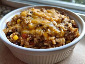 Close-up of a serving of cheesy mexican rice casserole topped with melted cheddar cheese in a white bowl.