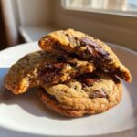 Close-up of chewy sourdough chocolate chip cookies, one broken open revealing melted chocolate.