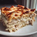 A hearty, layered slice of chicken alfredo lasagna featuring shredded chicken and creamy sauce, topped with perfectly browned cheese.