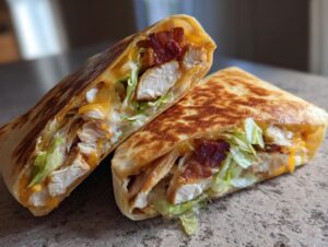 A grilled chicken bacon ranch wrap cut in half, showing layers of chicken, bacon, lettuce, and melted cheese.