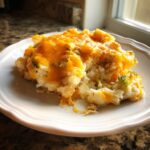 A close-up serving of cheesy chicken cauliflower rice casserole with visible broccoli florets on a white plate.