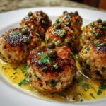 Close-up of seared chicken piccata meatballs topped with capers and parsley in a lemon butter sauce.