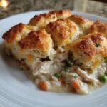 A scoop of creamy chicken pot pie casserole topped with golden, fluffy biscuits served on a white plate.
