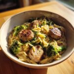 A bowl filled with creamy chicken sausage and broccoli orzo, topped with browned sausage pieces and fresh herbs.