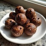 A pile of dark brown, textured protein balls studded with mini chocolate chips, resting on a white plate.