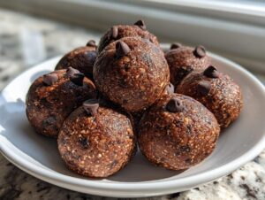 A close-up of several delicious chocolate chip protein balls piled on a white dish, ready for snacking.