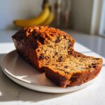 A freshly baked loaf of vegan banana bread with chocolate chips, sliced on a light plate.
