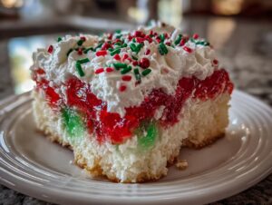A close-up of a slice of christmas poke cake featuring layers of red and green gelatin, white cake, and topped with whipped cream and holiday sprinkles.