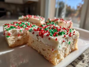 Four squares of soft christmas sugar cookie bars topped with thick white frosting and red and green sprinkles.