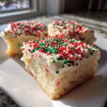 Three squares of soft christmas sugar cookie bars topped with white frosting and festive red, green, and white sprinkles.