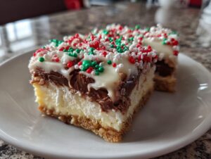 Two slices of rich Christmas tree cheesecake bars featuring a graham cracker crust, creamy filling, chocolate layer, and white frosting with red, green, and white sprinkles.
