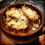 Close-up of a piping hot bowl of french onion soup topped with toasted bread and bubbly, melted Gruyère cheese.