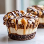 Close-up of a single cookie butter cheesecake cup topped with dripping caramel and chocolate sauce.