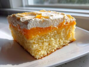 A close-up of a moist slice of Creamsicle Cake showing the yellow sponge, orange filling, and white topping.