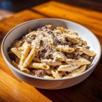 A close-up of a bowl filled with creamy beef pasta, penne coated in a rich sauce and topped with ground beef and grated Parmesan.
