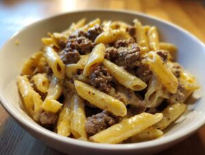 Close-up of a white bowl filled with creamy beef pasta made with penne noodles and ground beef.