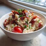 A white bowl filled with creamy blt chicken salad, topped with crispy bacon bits and fresh parsley.