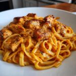 Close-up of creamy pasta topped with seasoned, cubed cajun chicken pieces.