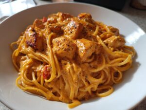 Close-up of creamy pasta tossed with chunks of seasoned cajun chicken in a white bowl.