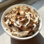 A close-up of creamy caramelized onion dip, topped generously with dark, sweet caramelized onions, served in a white bowl.