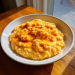 A close-up of a white bowl filled with creamy, bright orange cheese grits, seasoned with pepper.