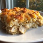 A close-up of a creamy slice of chicken and rice casserole topped with melted cheddar and herbs.