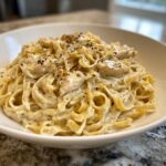 A close-up of a generous serving of creamy chicken fettuccine alfredo pasta, topped with cracked black pepper.