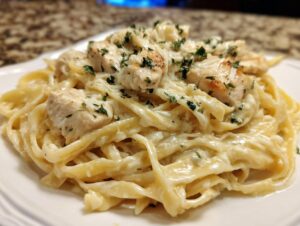 A close-up of creamy chicken fettuccine alfredo pasta topped with shredded cheese and fresh parsley.