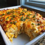 A baked, creamy corn dip topped with melted cheddar cheese and green onions, with a scoop removed.