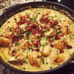Close-up of creamy crack chicken gnocchi in a skillet, topped with bacon bits and fresh chives.