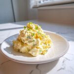 A serving of creamy egg salad recipe, topped with fresh chopped green onions, on a white plate.
